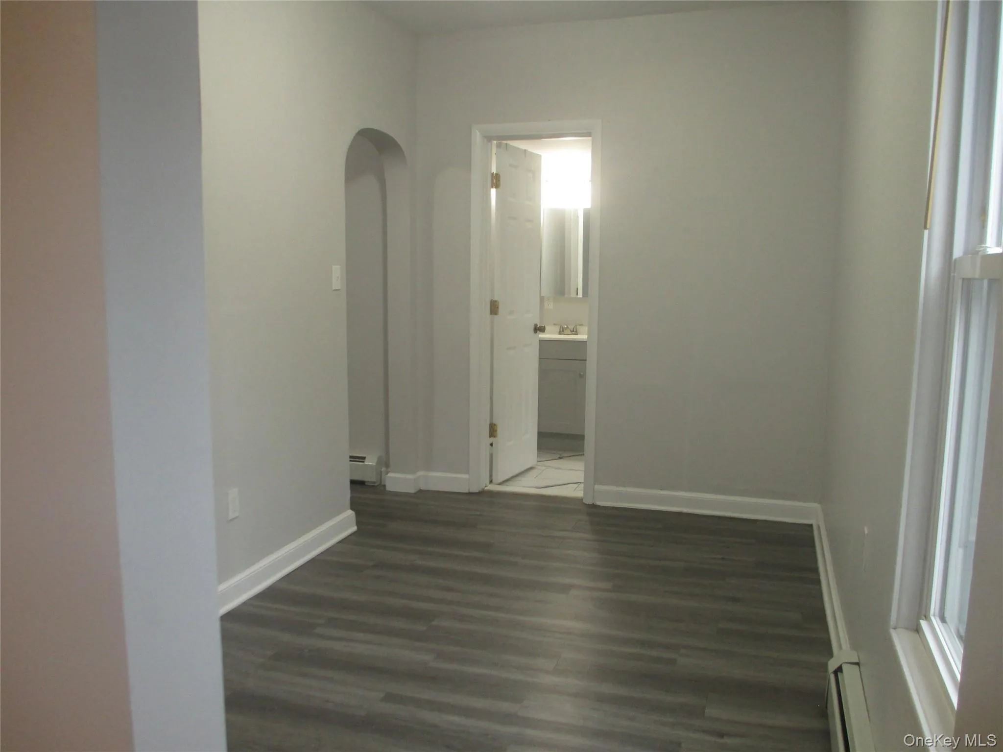 Empty room featuring dark wood finished floors, arched walkways, and a baseboard radiator Empty room featuring dark wood finished floors, arched walkways, and a baseboard radiator