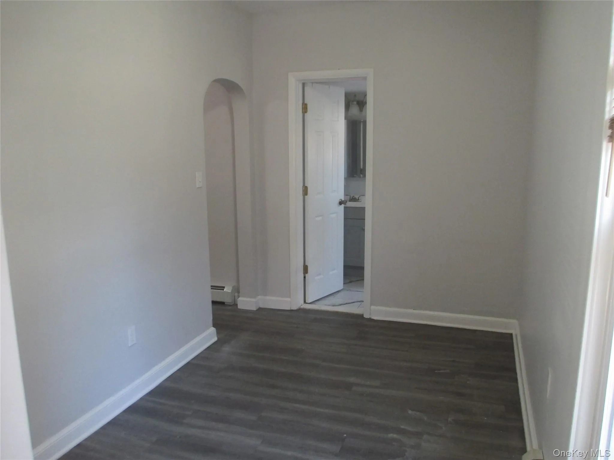 Empty room with dark wood-style floors, arched walkways, and a baseboard heating unit Empty room with dark wood-style floors, arched walkways, and a baseboard heating unit