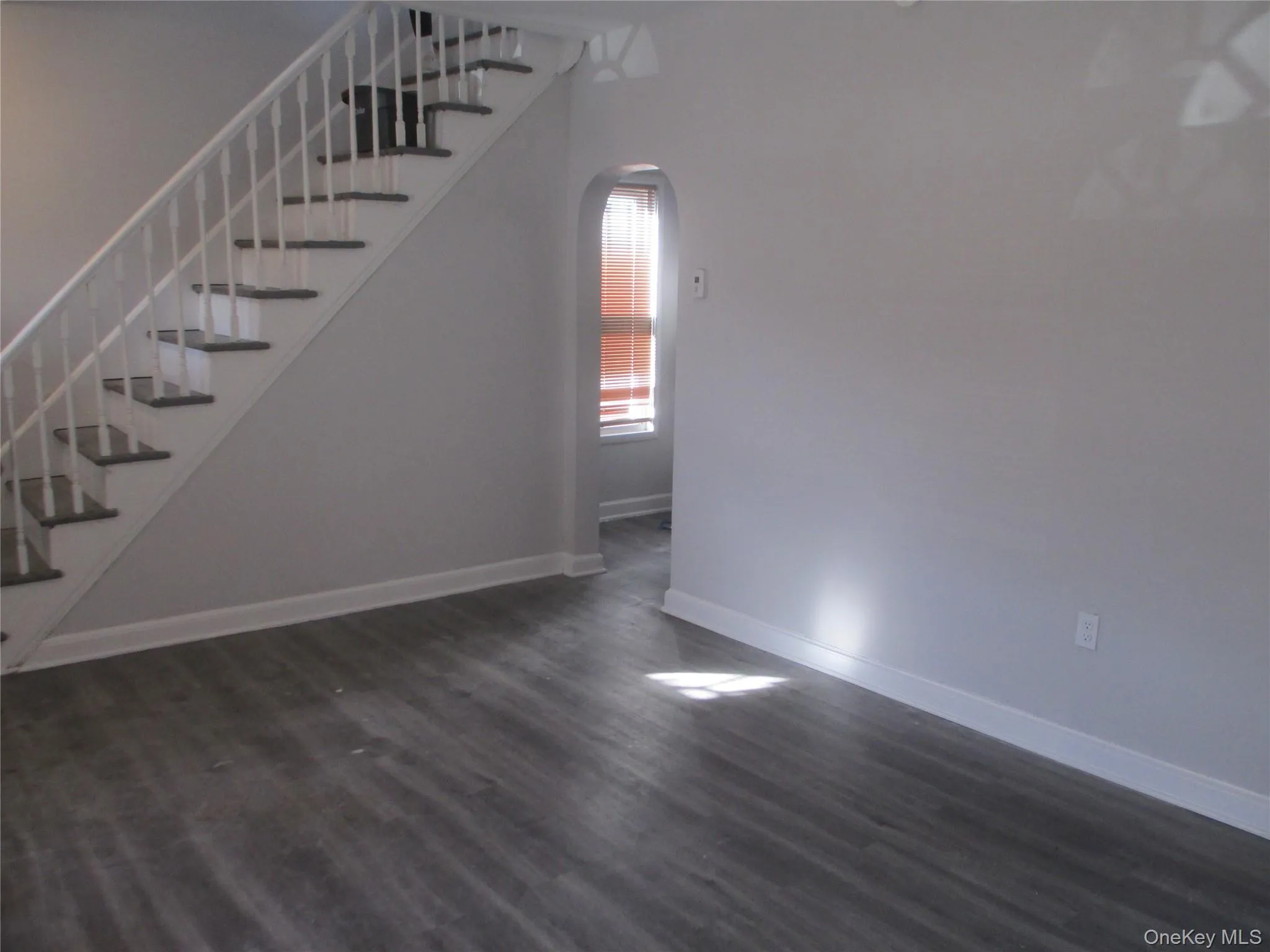 Unfurnished living room featuring stairs, arched walkways, and dark wood-type flooring Unfurnished living room featuring stairs, arched walkways, and dark wood-type flooring