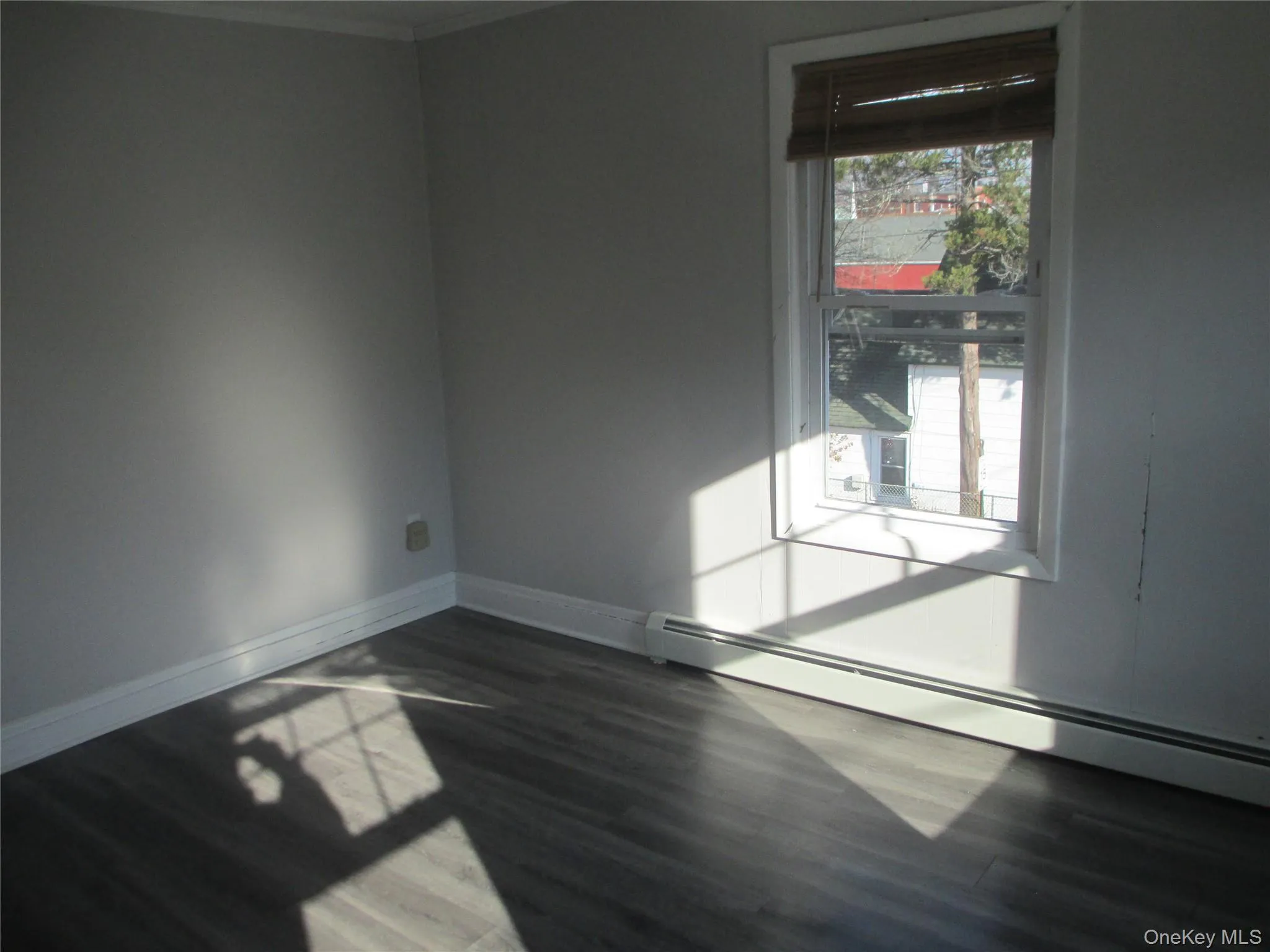 Unfurnished room with a baseboard heating unit and dark wood-style floors Unfurnished room with a baseboard heating unit and dark wood-style floors