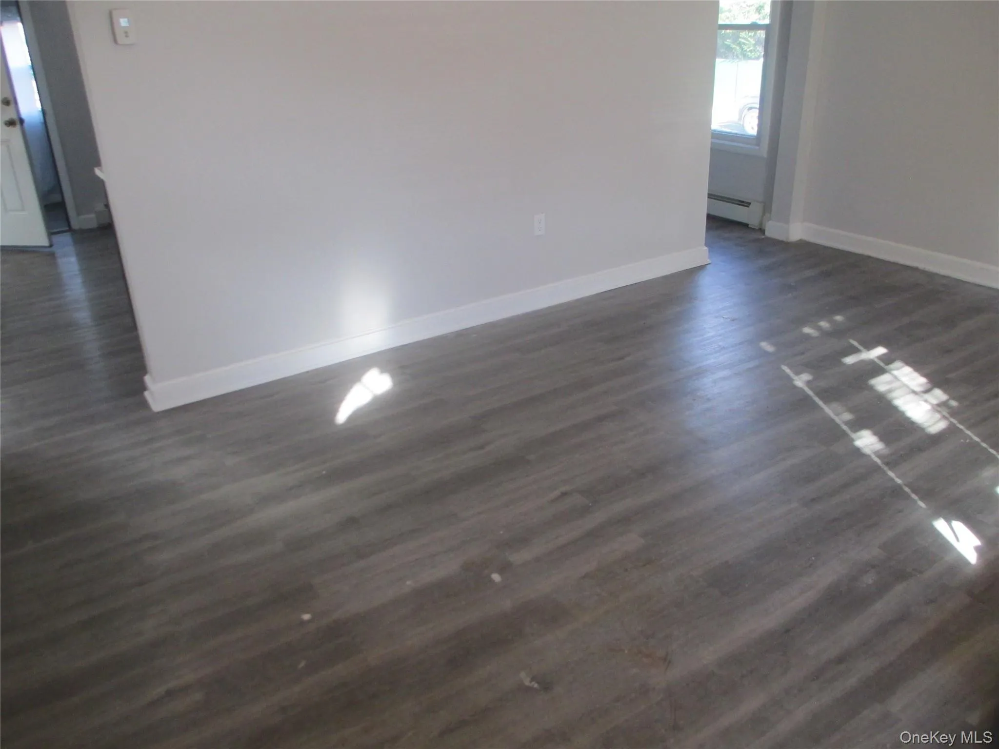 Empty room featuring dark wood-style flooring and baseboard heating Empty room featuring dark wood-style flooring and baseboard heating
