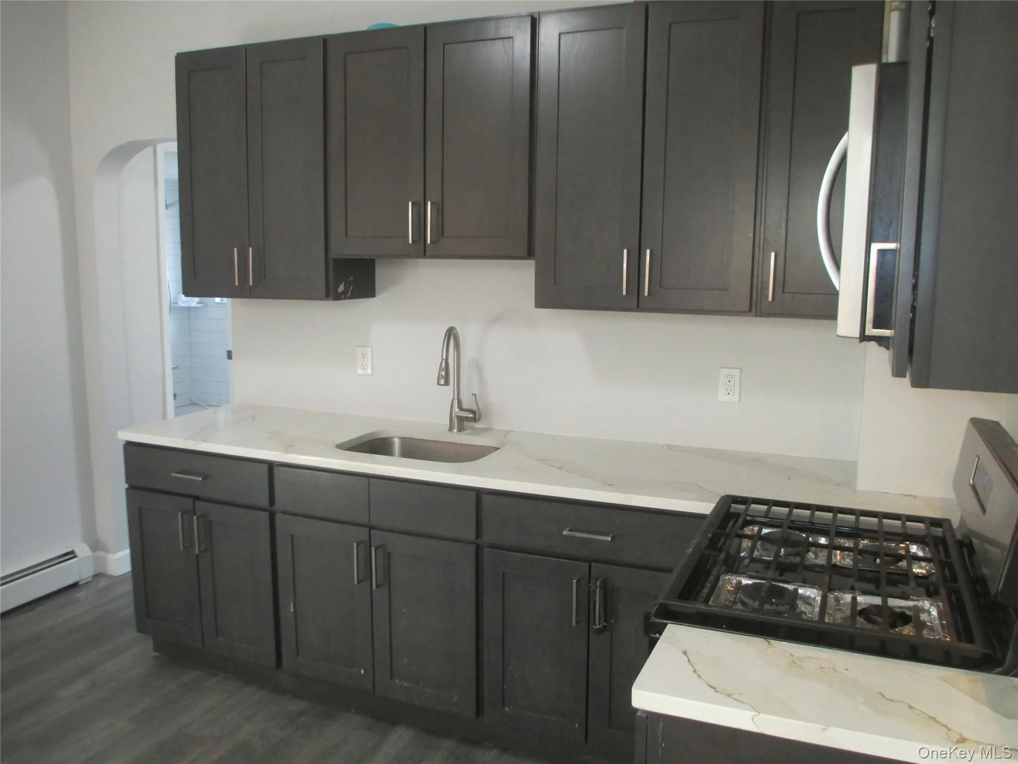 Kitchen featuring gas range oven, light stone counters, dark wood-type flooring, and stainless steel microwave Kitchen featuring gas range oven, light stone counters, dark wood-type flooring, and stainless steel microwave