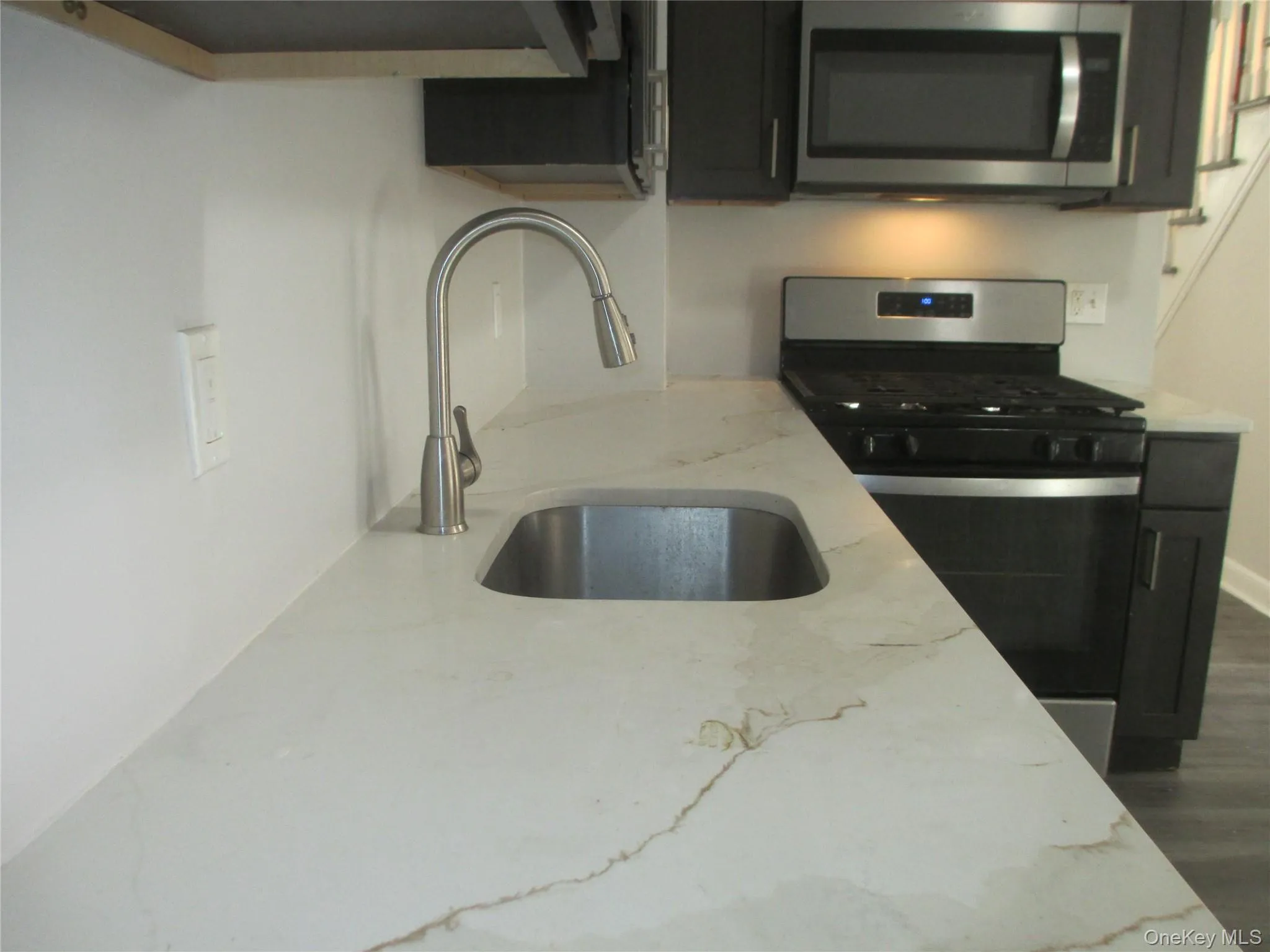 Kitchen with stainless steel appliances, light stone counters, and dark wood finished floors Kitchen with stainless steel appliances, light stone counters, and dark wood finished floors