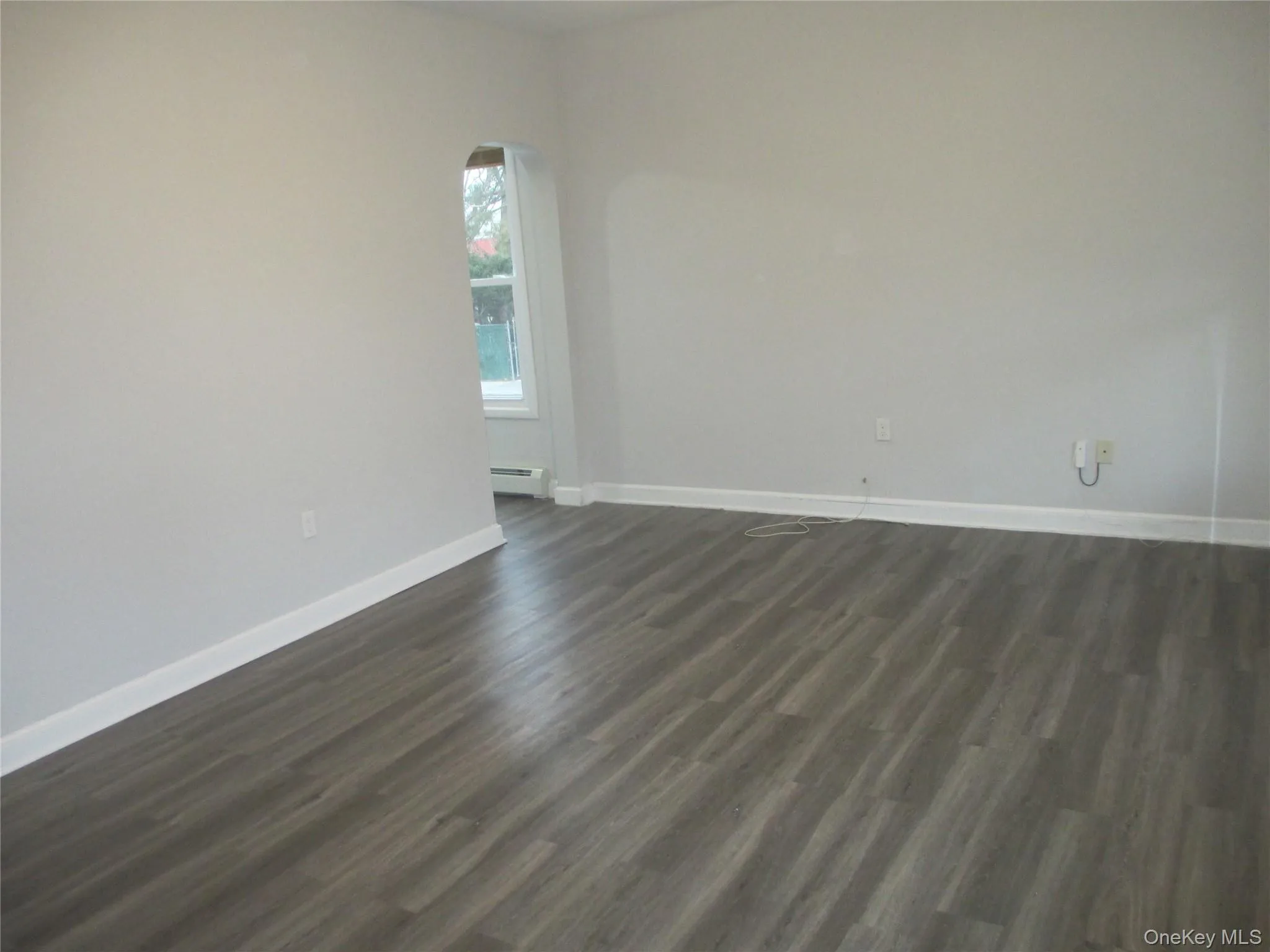Spare room with dark wood-type flooring and a baseboard heating unit Spare room with dark wood-type flooring and a baseboard heating unit