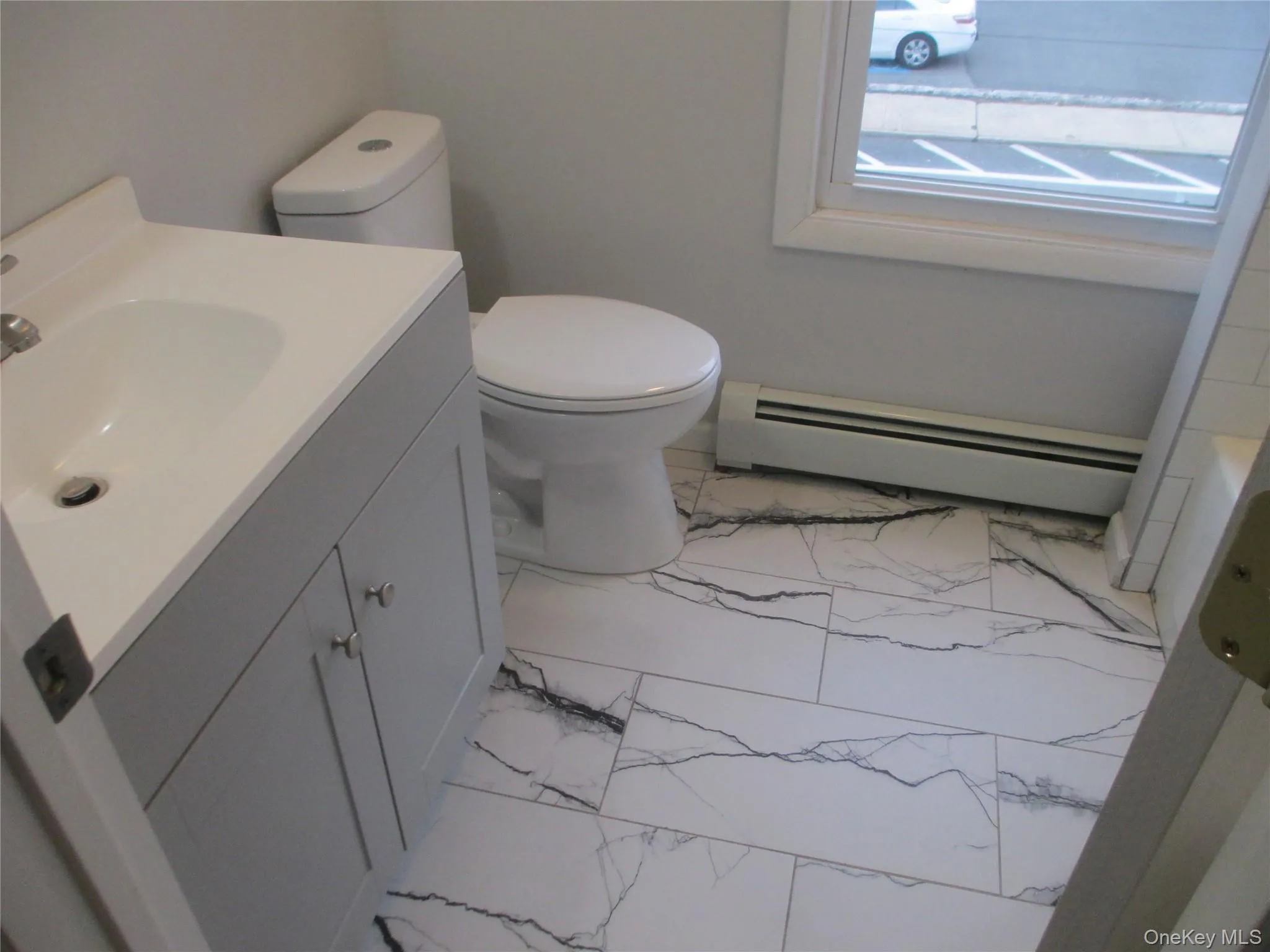 Bathroom with light marble finish flooring, vanity, and a baseboard heating unit Bathroom with light marble finish flooring, vanity, and a baseboard heating unit