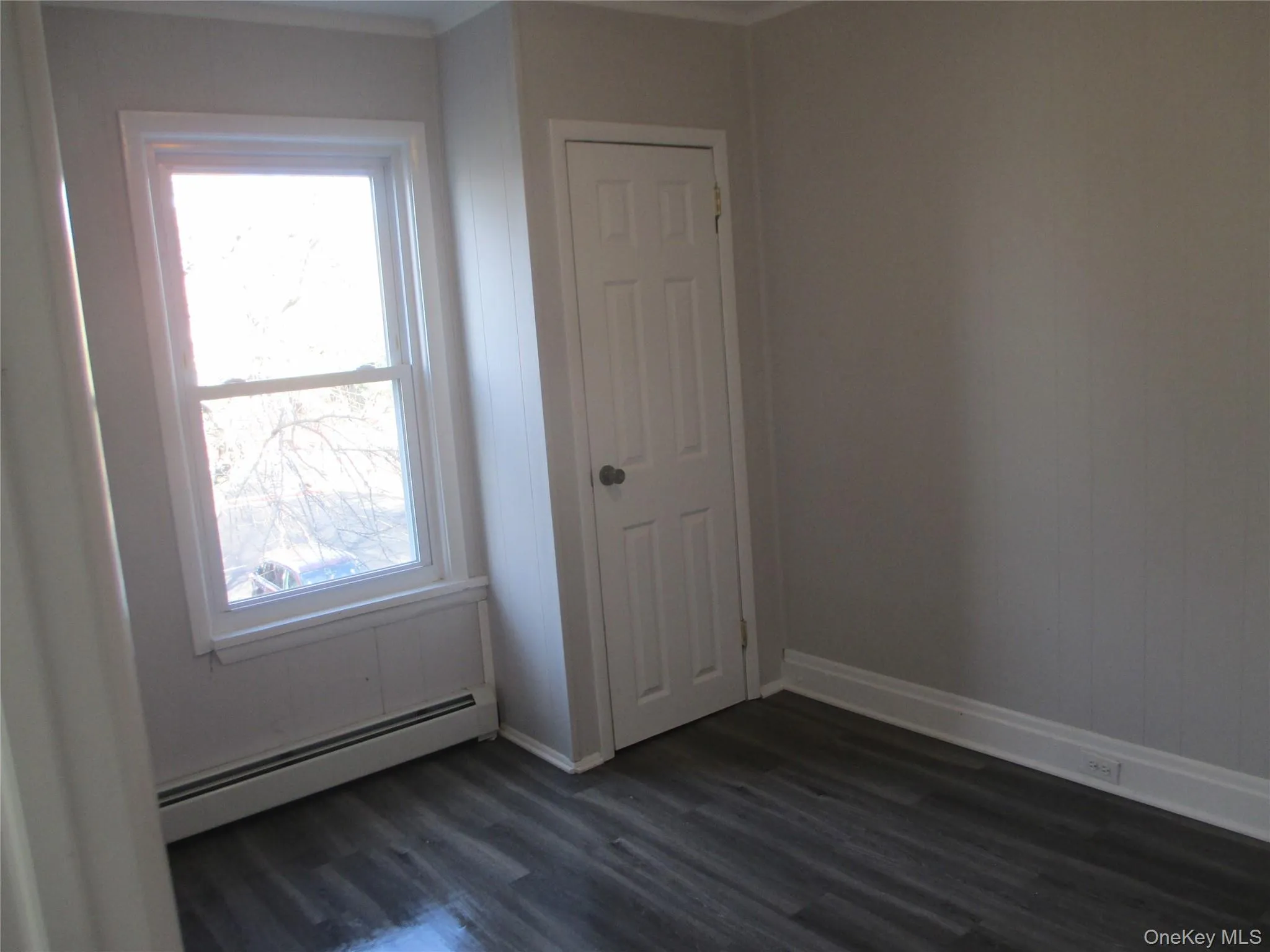 Empty room featuring a baseboard heating unit and dark wood finished floors Empty room featuring a baseboard heating unit and dark wood finished floors