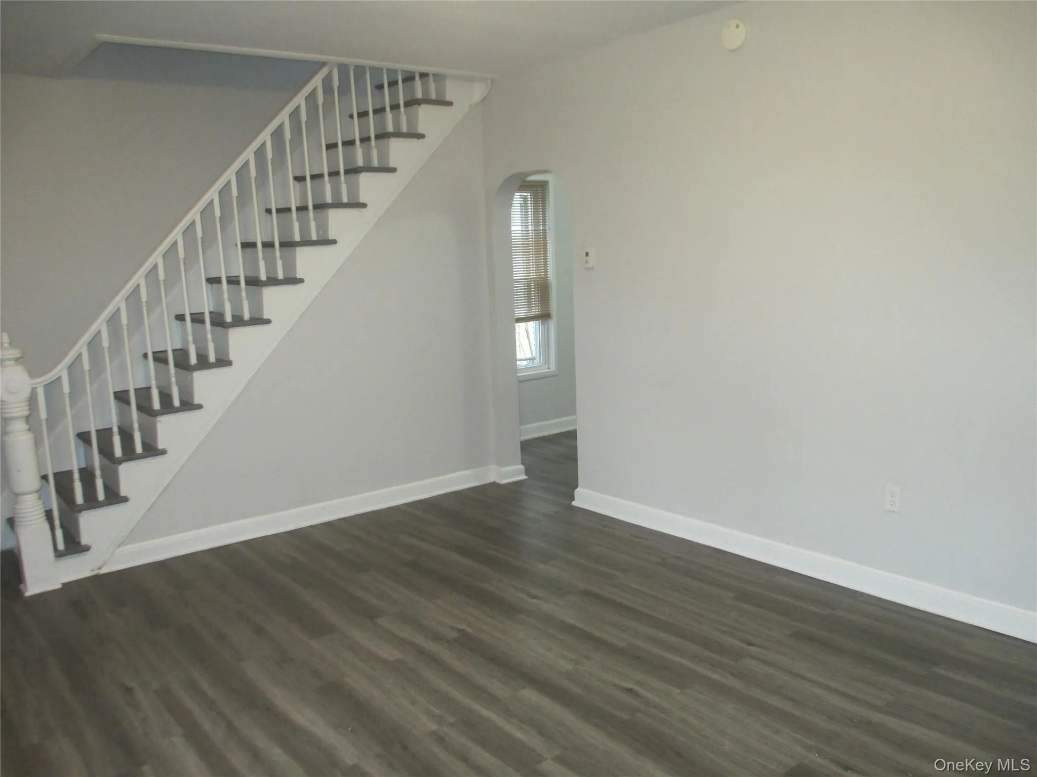 Unfurnished living room with stairs, dark wood-style floors, and arched walkways Unfurnished living room with stairs, dark wood-style floors, and arched walkways
