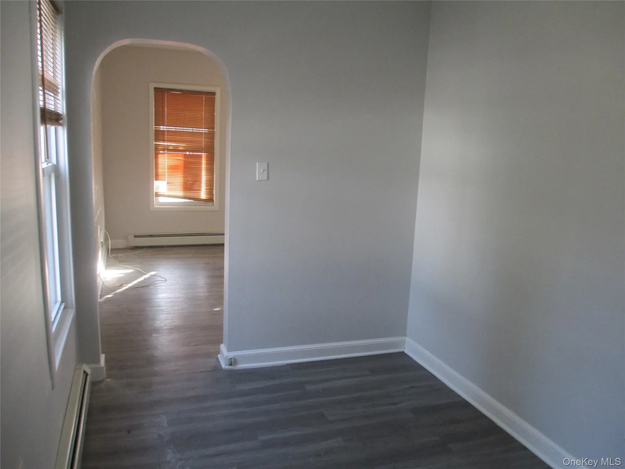 Unfurnished room with dark wood-style flooring, a baseboard radiator, and arched walkways Unfurnished room with dark wood-style flooring, a baseboard radiator, and arched walkways