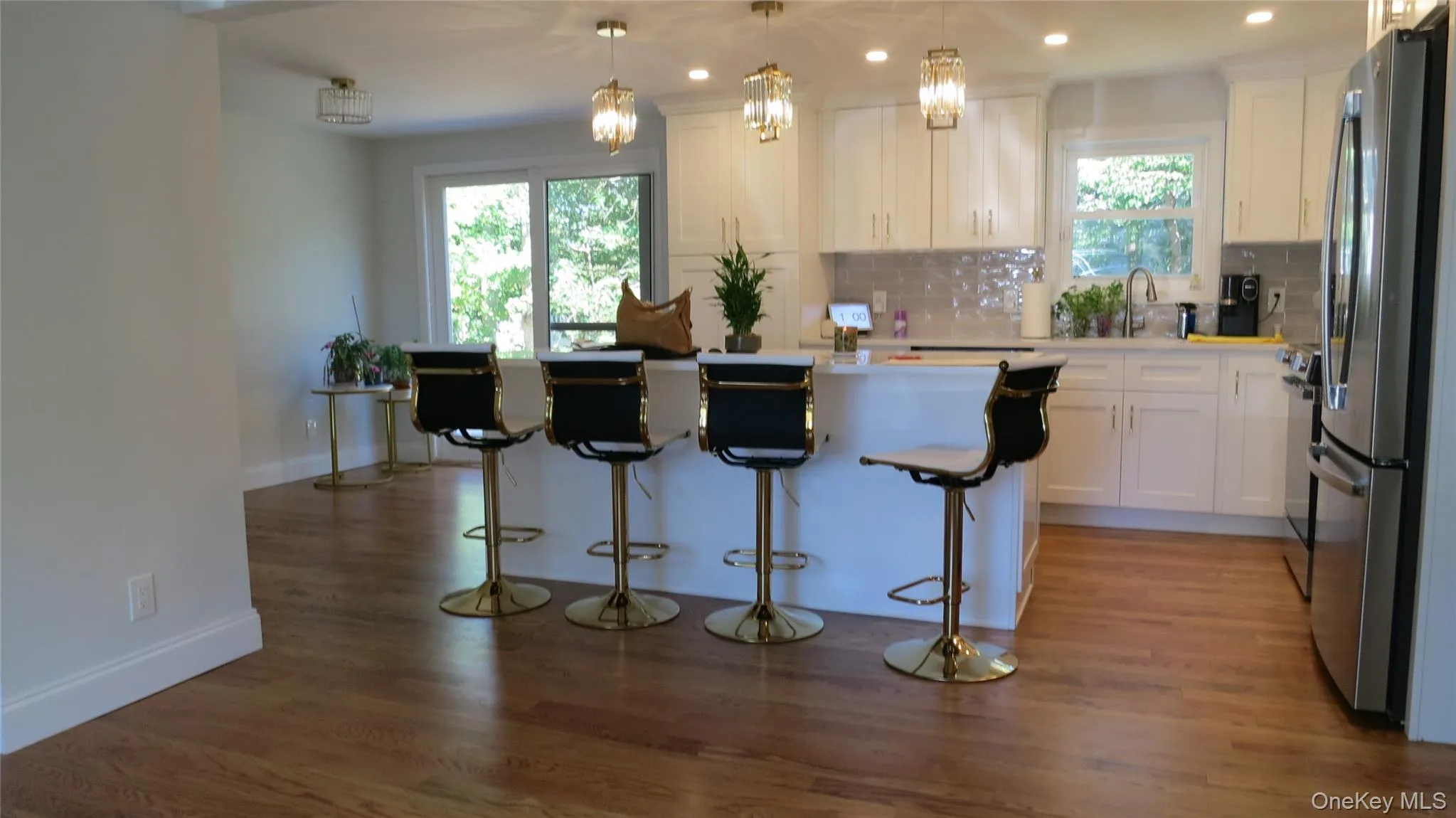 Kitchen with backsplash, decorative light fixtures, dark wood-style flooring, white cabinets, and light countertops Kitchen with backsplash, decorative light fixtures, dark wood-style flooring, white cabinets, and light countertops