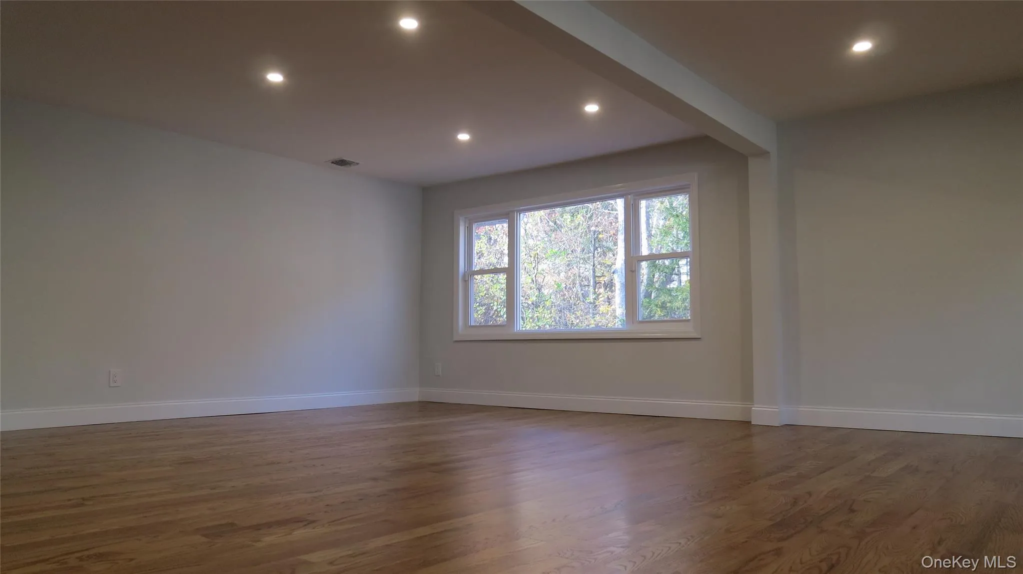 Empty room with dark wood-style floors, beamed ceiling, and recessed lighting Empty room with dark wood-style floors, beamed ceiling, and recessed lighting