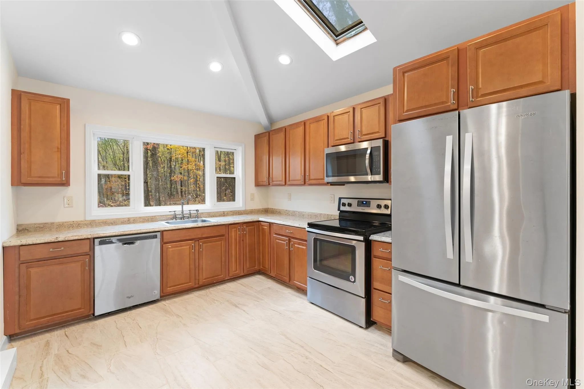 54 De Liso: Kitchen with stainless steel appliances, vaulted ceiling, a skylight, brown cabinetry, and recessed lighting 54 De Liso: Kitchen with stainless steel appliances, vaulted ceiling, a skylight, brown cabinetry, and recessed lighting