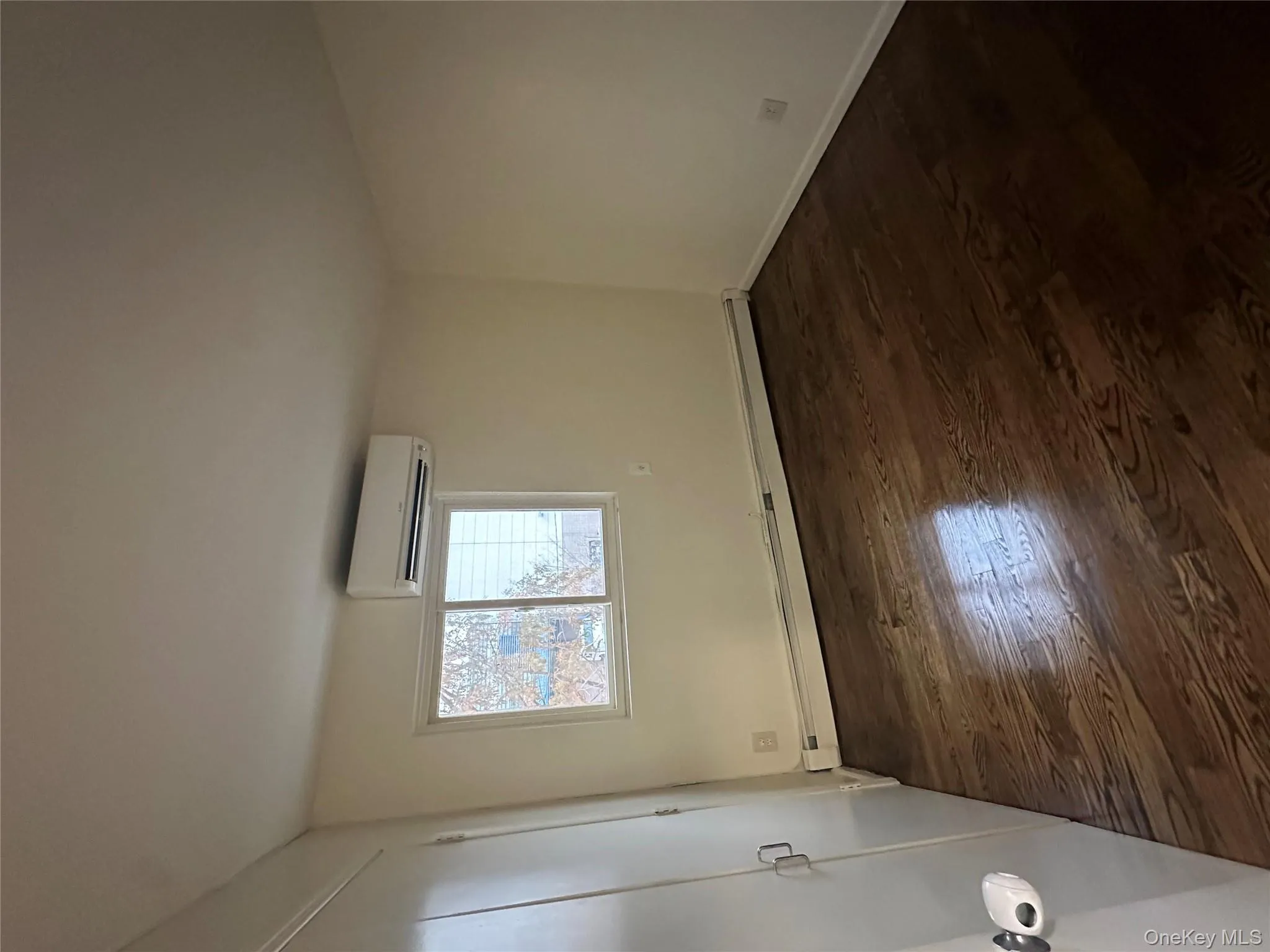 Unfurnished bedroom with dark wood-type flooring, baseboard heating, a wall unit AC, and a closet Unfurnished bedroom with dark wood-type flooring, baseboard heating, a wall unit AC, and a closet