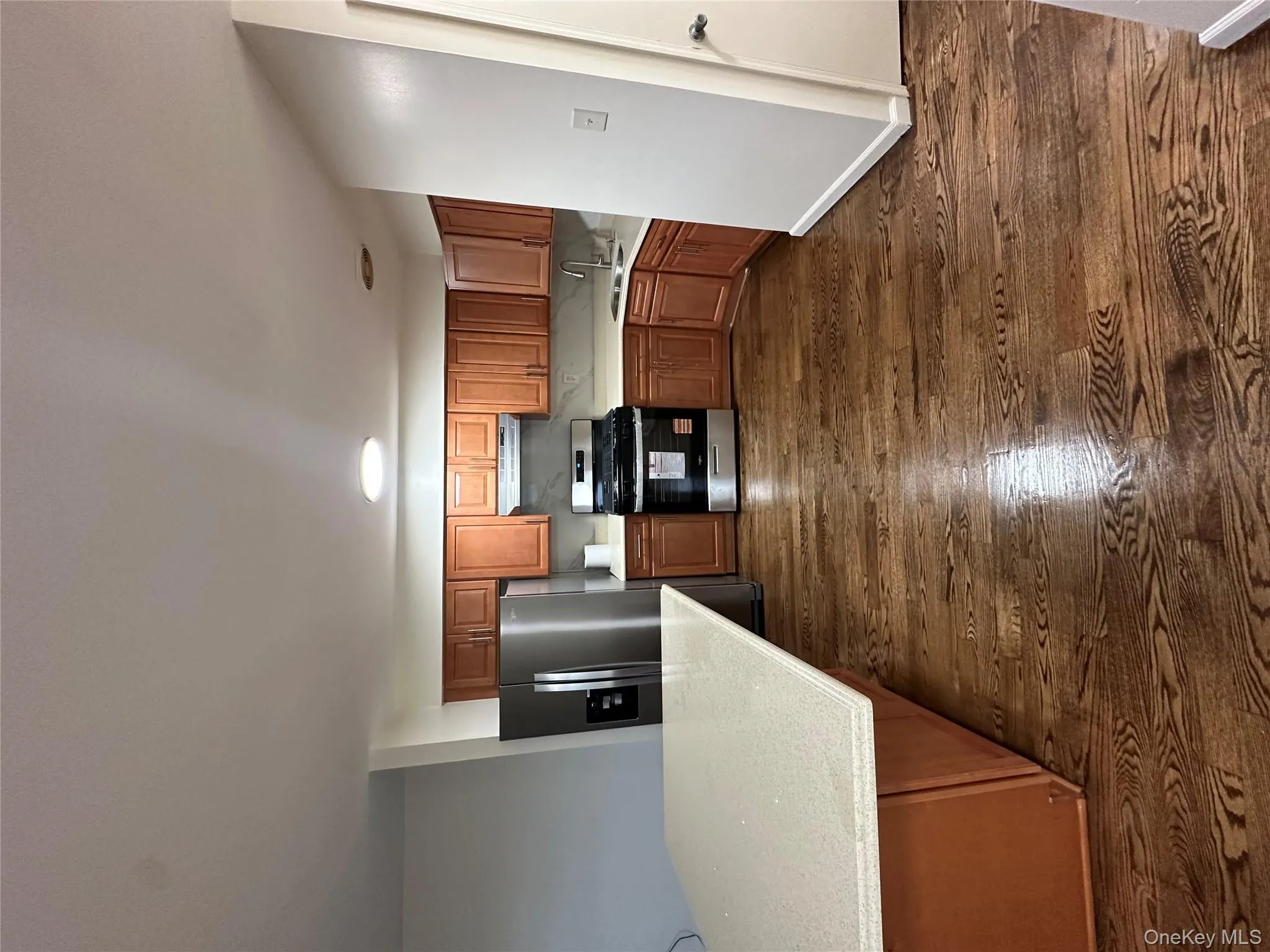 Kitchen featuring brown cabinetry, gas range, fridge, dark wood-style floors, and light stone countertops Kitchen featuring brown cabinetry, gas range, fridge, dark wood-style floors, and light stone countertops