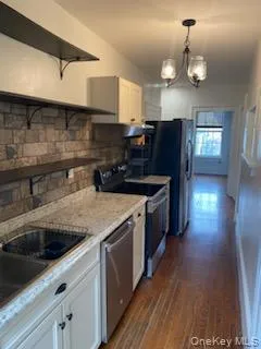 Kitchen featuring open shelves, white cabinets, appliances with stainless steel finishes, dark wood-type flooring, and a chandelier Kitchen featuring open shelves, white cabinets, appliances with stainless steel finishes, dark wood-type flooring, and a chandelier