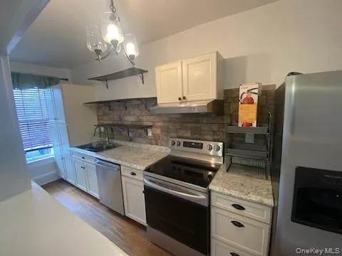 Kitchen with appliances with stainless steel finishes, white cabinets, open shelves, dark wood-style flooring, and backsplash Kitchen with appliances with stainless steel finishes, white cabinets, open shelves, dark wood-style flooring, and backsplash