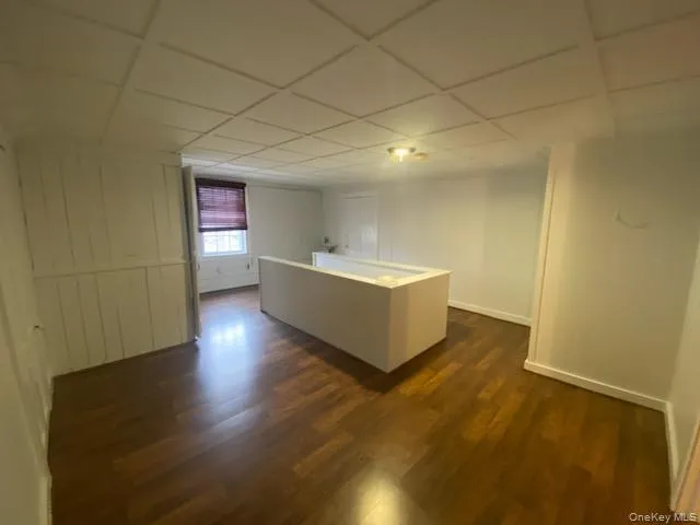 Kitchen featuring dark wood finished floors, a center island, light countertops, a paneled ceiling, and white cabinetry Kitchen featuring dark wood finished floors, a center island, light countertops, a paneled ceiling, and white cabinetry