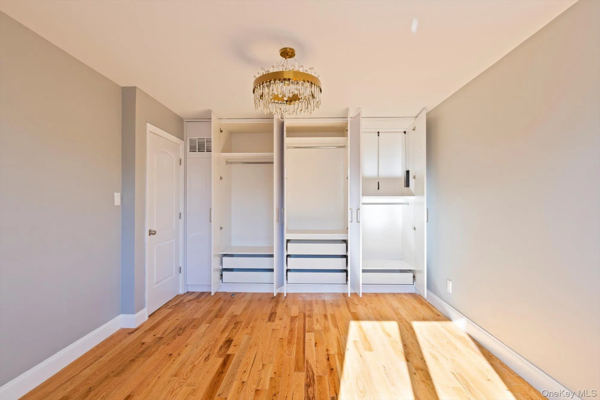 Unfurnished bedroom with light wood-style flooring, multiple closets, and a chandelier Unfurnished bedroom with light wood-style flooring, multiple closets, and a chandelier