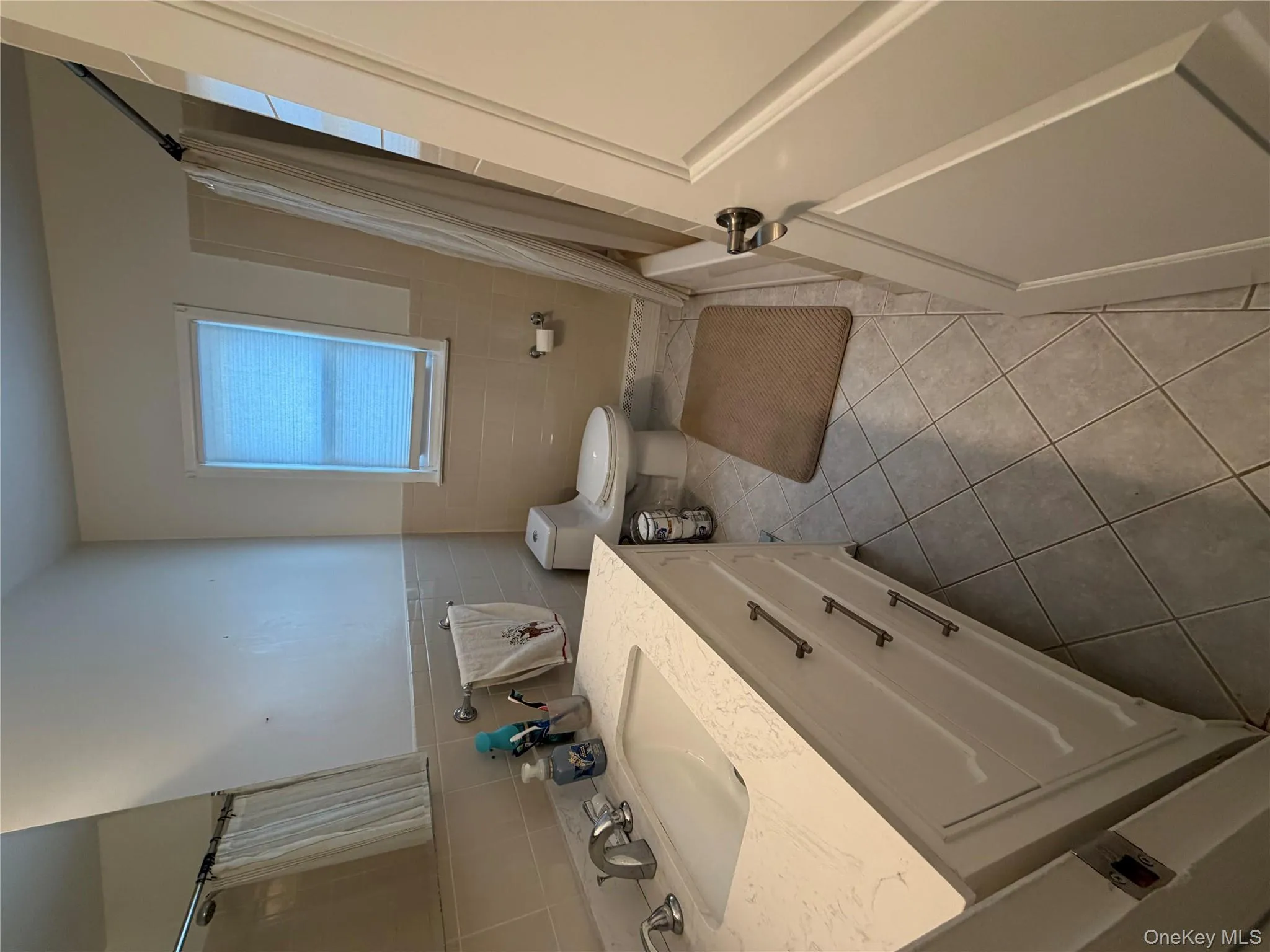 Bathroom with vanity, light tile patterned floors, tile walls, shower / bathtub combination with curtain, and a wainscoted wall Bathroom with vanity, light tile patterned floors, tile walls, shower / bathtub combination with curtain, and a wainscoted wall