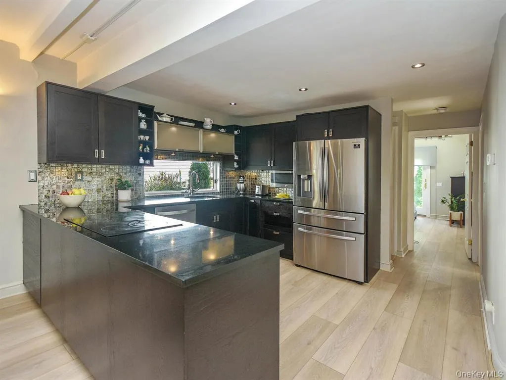Kitchen featuring appliances with stainless steel finishes, dark cabinetry, backsplash, a peninsula, and light wood finished floors Kitchen featuring appliances with stainless steel finishes, dark cabinetry, backsplash, a peninsula, and light wood finished floors