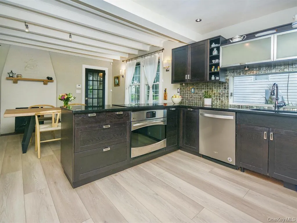 Kitchen with open shelves, beam ceiling, stainless steel appliances, decorative backsplash, and light wood-style flooring Kitchen with open shelves, beam ceiling, stainless steel appliances, decorative backsplash, and light wood-style flooring