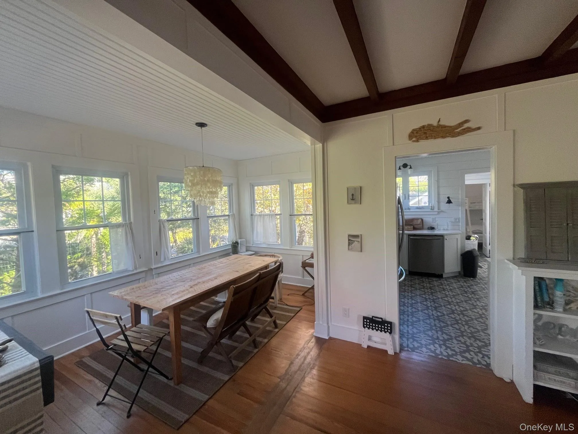 Dining room featuring dark wood-style floors, a decorative wall, and beamed ceiling Dining room featuring dark wood-style floors, a decorative wall, and beamed ceiling