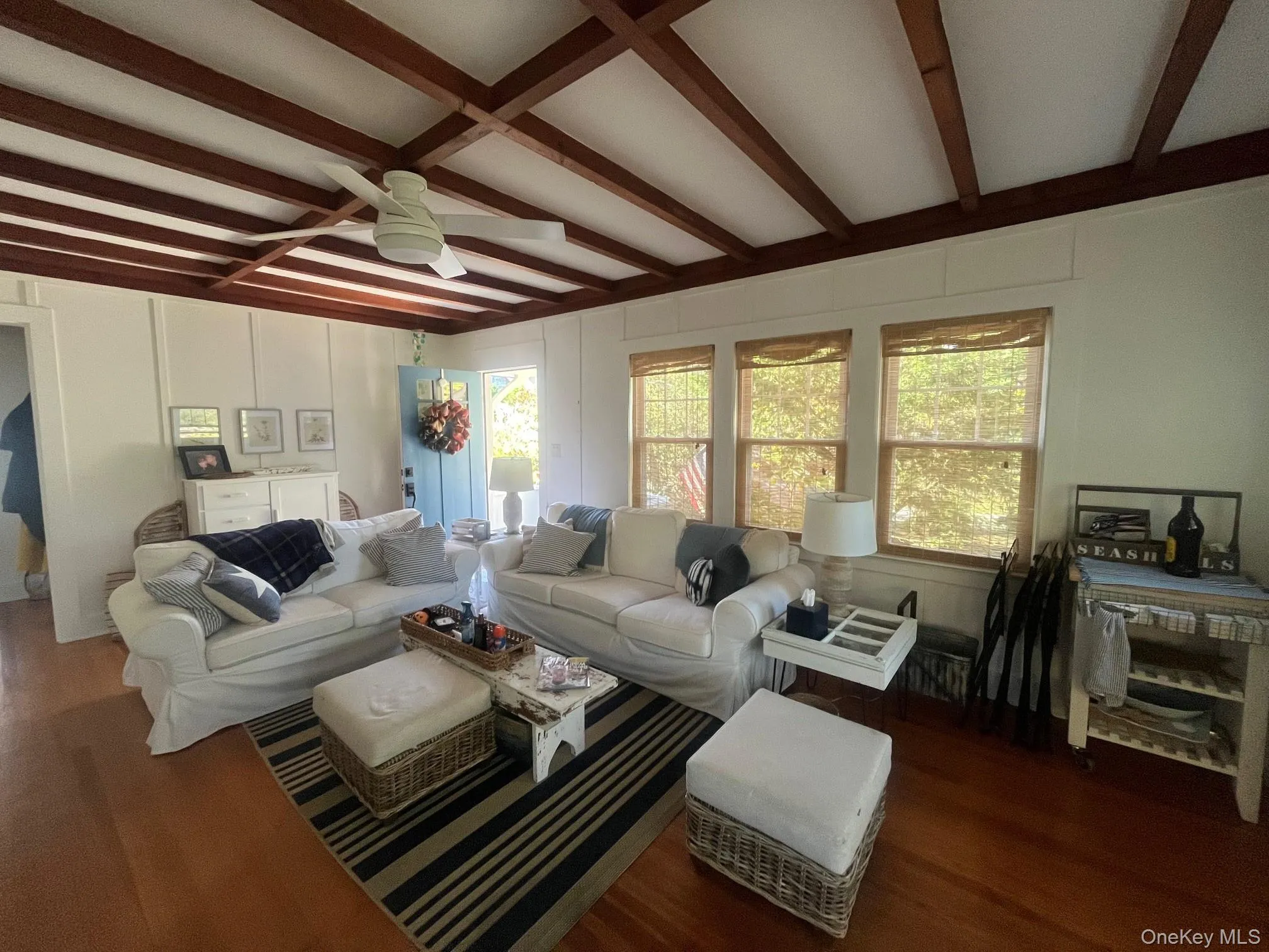 Living area featuring beamed ceiling, dark wood-type flooring, plenty of natural light, ceiling fan, and a decorative wall Living area featuring beamed ceiling, dark wood-type flooring, plenty of natural light, ceiling fan, and a decorative wall