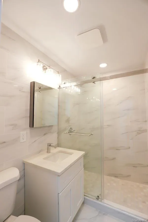 Bathroom with tile walls, vanity, a marble finish shower, light marble finish flooring, and recessed lighting Bathroom with tile walls, vanity, a marble finish shower, light marble finish flooring, and recessed lighting