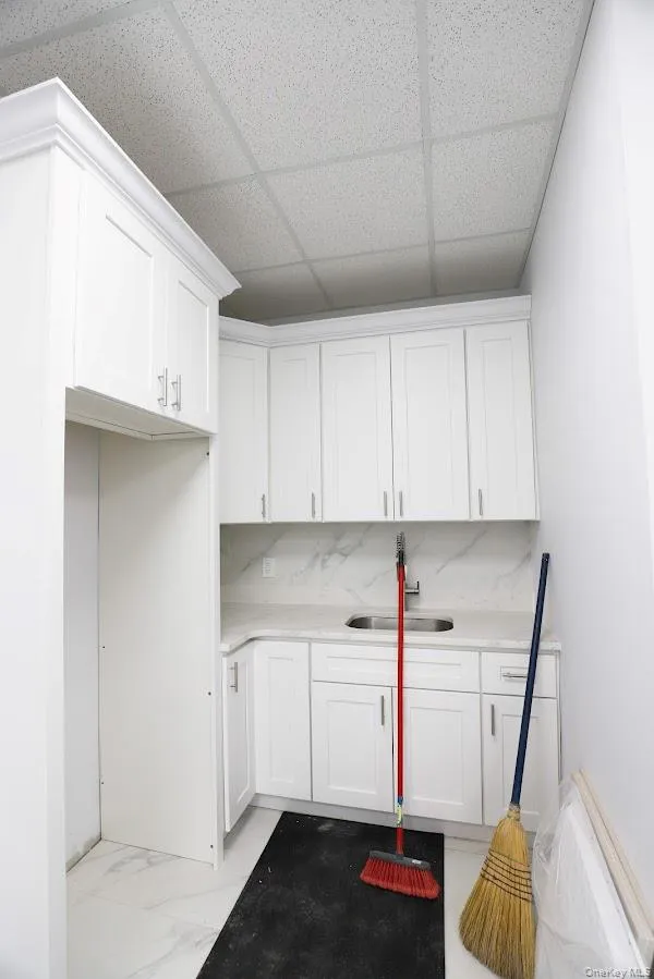 Kitchen with light marble finish floors, white cabinetry, a drop ceiling, and light stone countertops Kitchen with light marble finish floors, white cabinetry, a drop ceiling, and light stone countertops