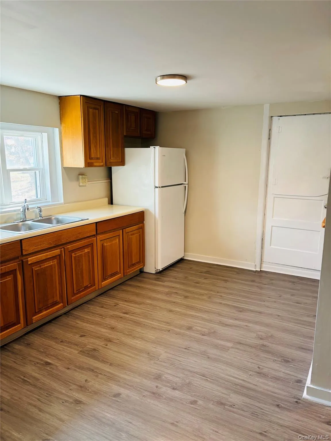 Kitchen featuring light countertops, light wood finished floors, freestanding refrigerator, and brown cabinets Kitchen featuring light countertops, light wood finished floors, freestanding refrigerator, and brown cabinets