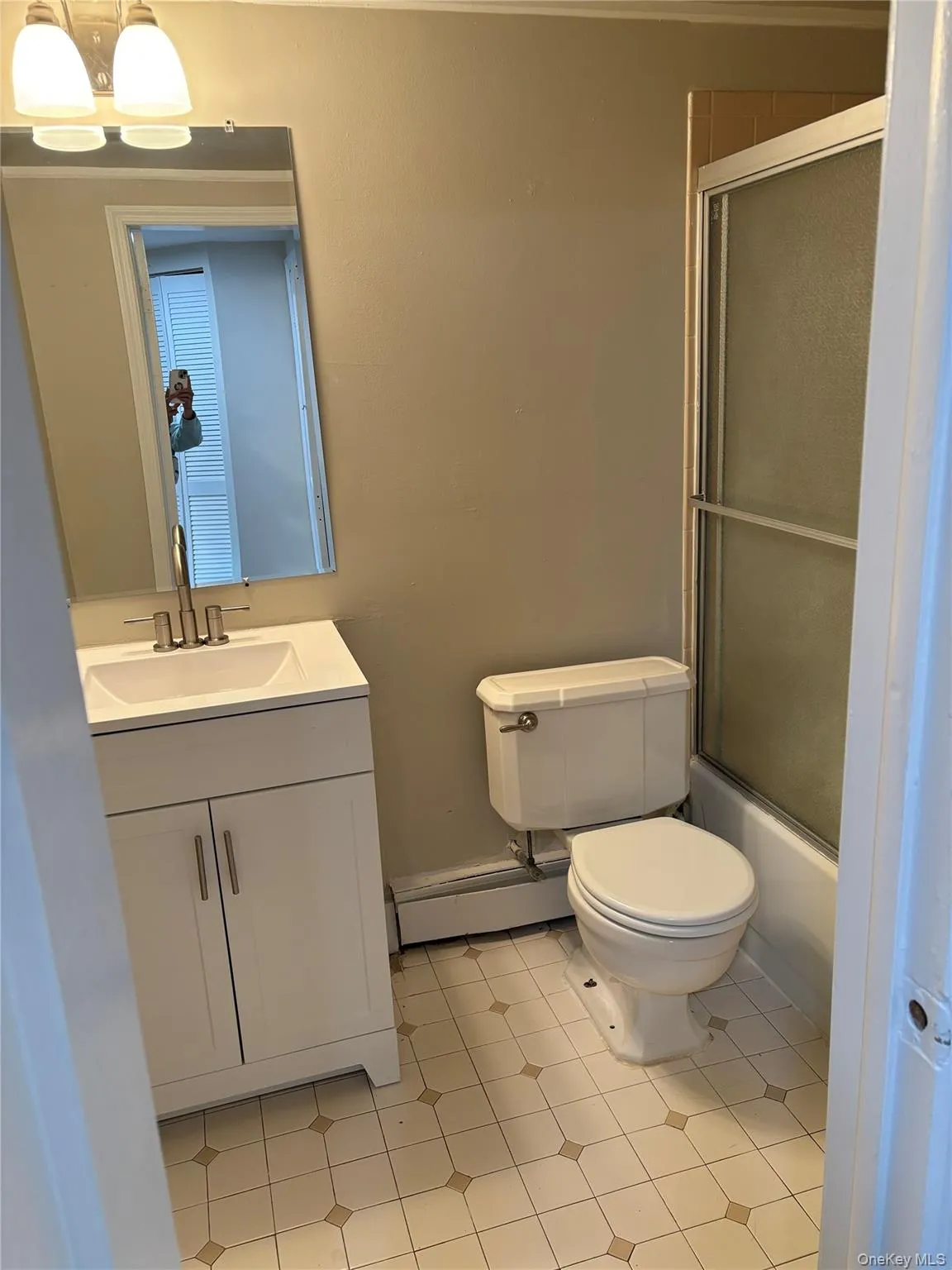 Bathroom with vanity, combined bath / shower with glass door, baseboard heating, and light tile patterned floors Bathroom with vanity, combined bath / shower with glass door, baseboard heating, and light tile patterned floors