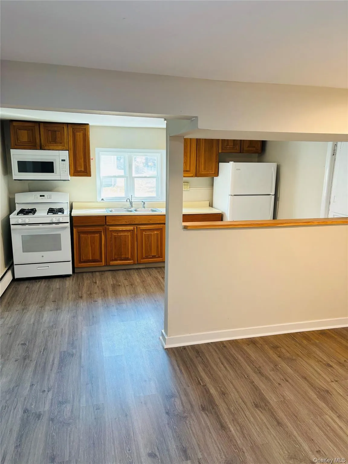 Kitchen featuring white appliances, brown cabinetry, light countertops, dark wood-style floors, and a baseboard heating unit Kitchen featuring white appliances, brown cabinetry, light countertops, dark wood-style floors, and a baseboard heating unit