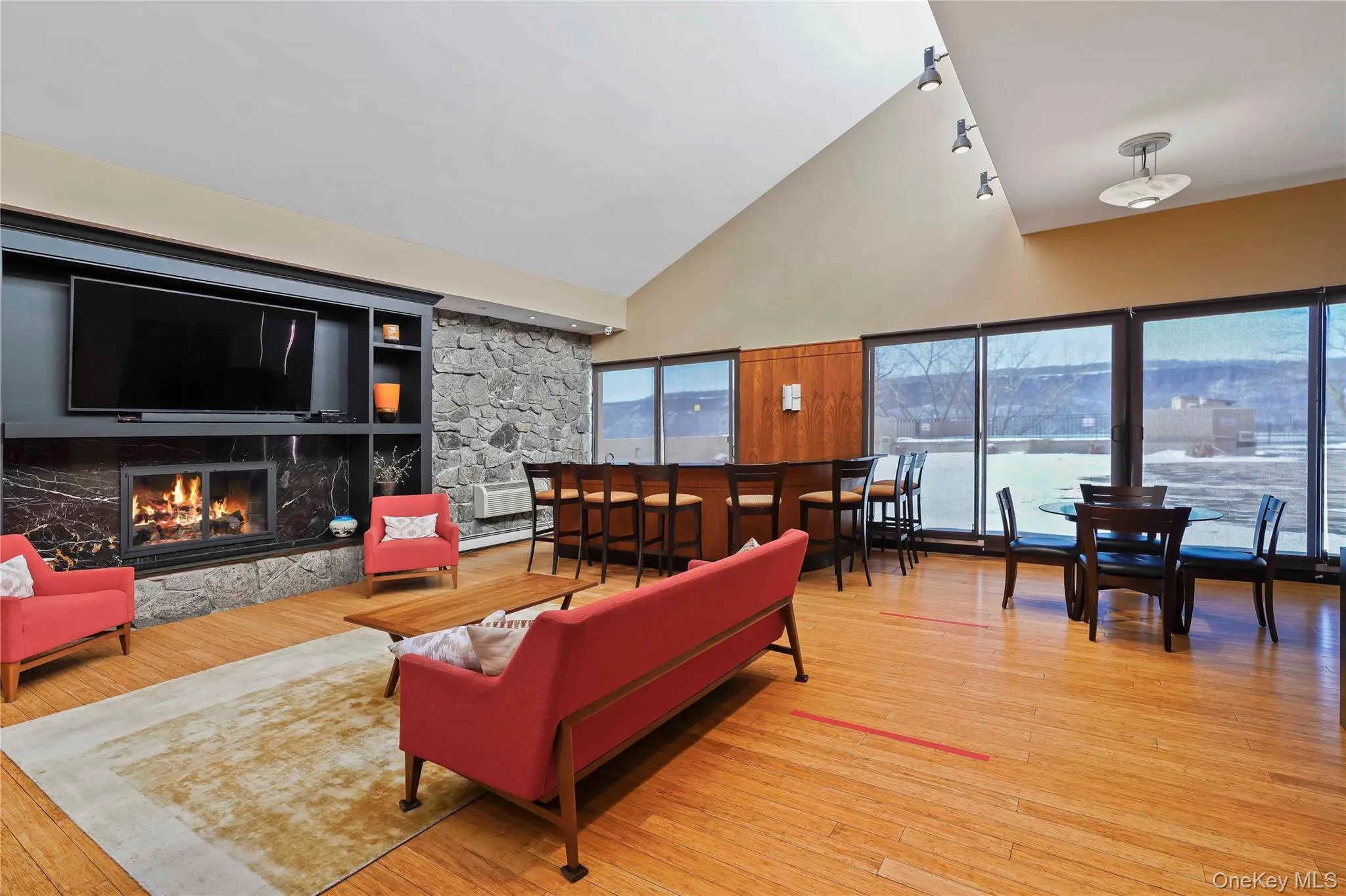 Recreation room featuring high vaulted ceiling, light wood finished floors, a premium fireplace, and a baseboard heating unit Recreation room featuring high vaulted ceiling, light wood finished floors, a premium fireplace, and a baseboard heating unit