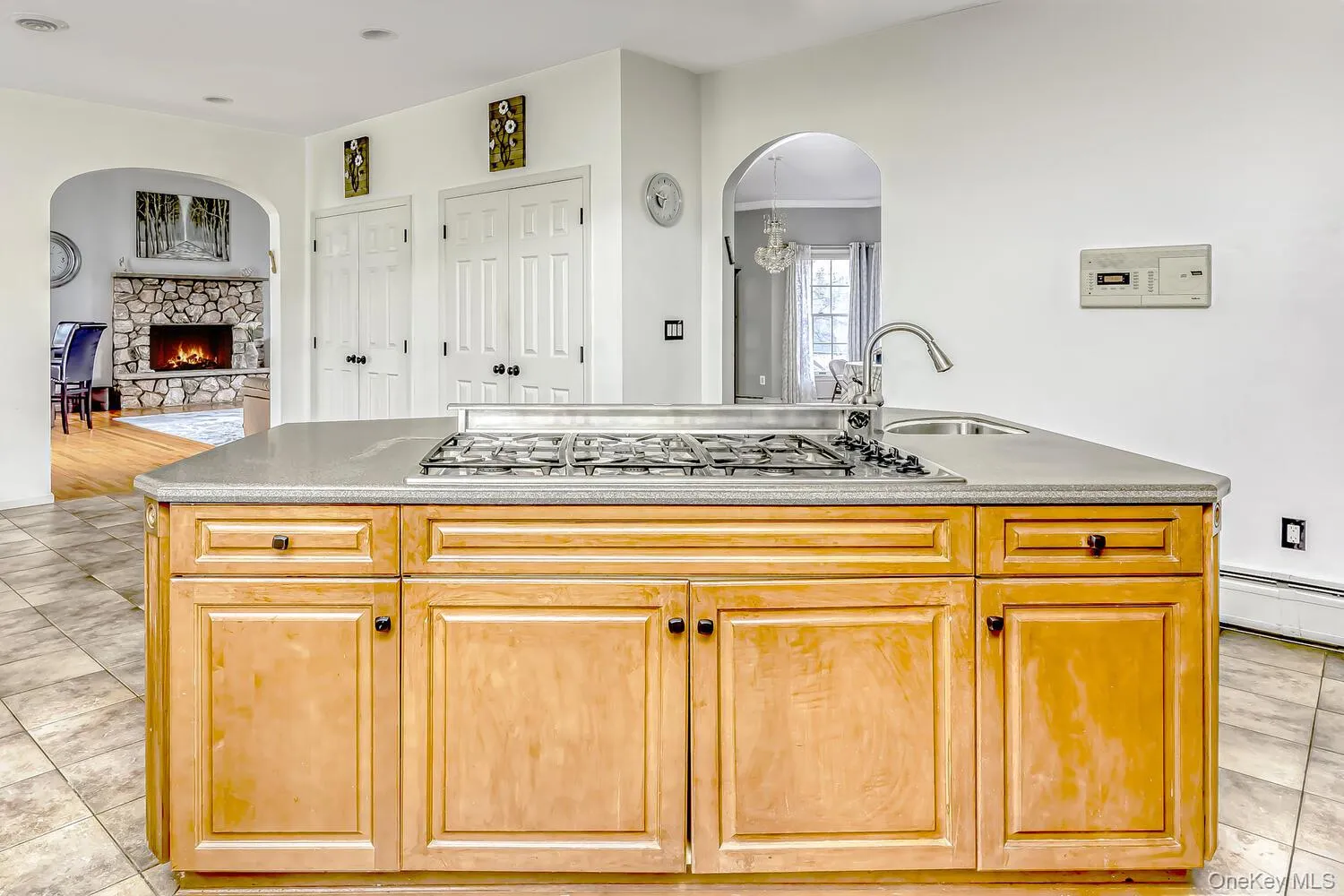 Kitchen featuring light tile patterned floors, arched walkways, an island with sink, light brown cabinets, and open floor plan Kitchen featuring light tile patterned floors, arched walkways, an island with sink, light brown cabinets, and open floor plan