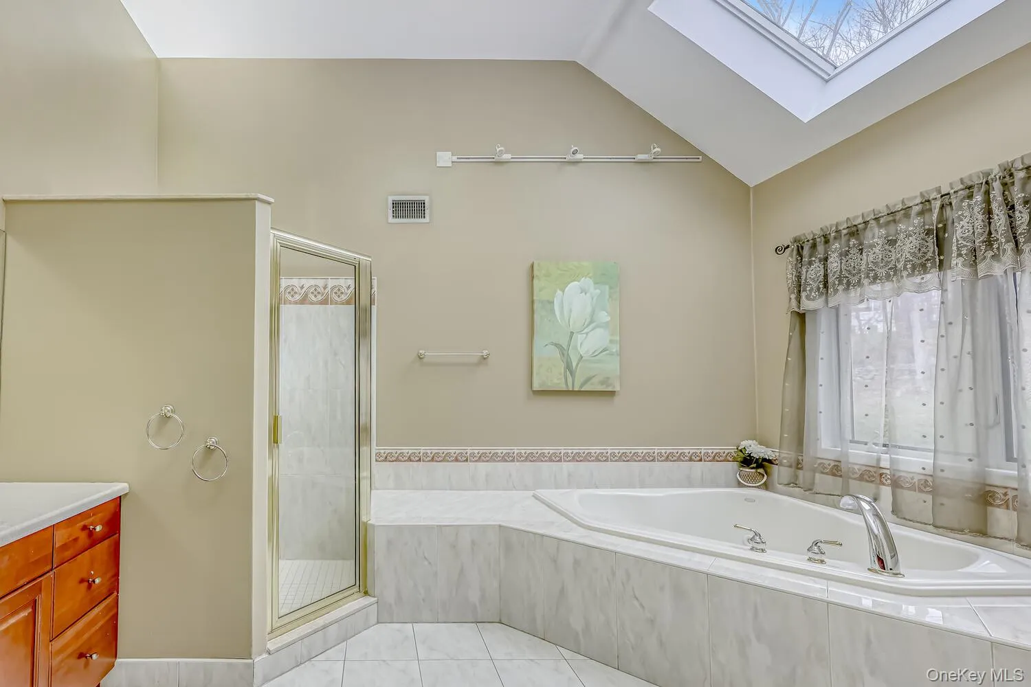 Bathroom featuring a skylight, a bath, a shower stall, light tile patterned floors, and lofted ceiling Bathroom featuring a skylight, a bath, a shower stall, light tile patterned floors, and lofted ceiling
