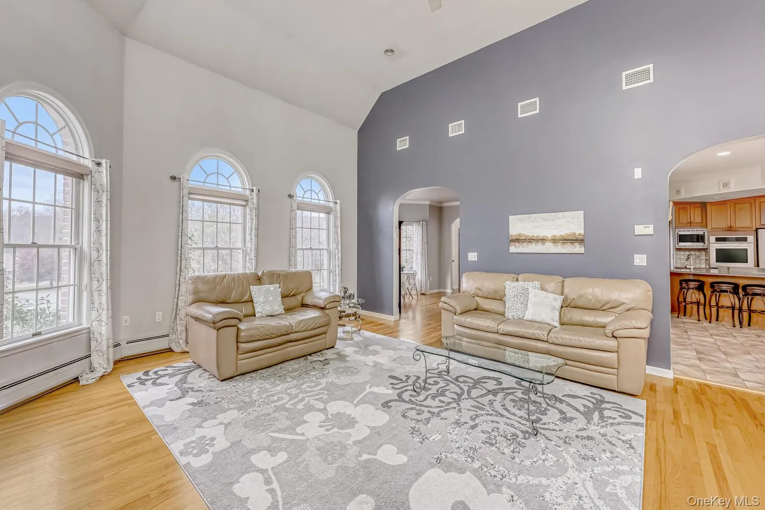 Living area with arched walkways, high vaulted ceiling, light wood-style flooring, and baseboard heating Living area with arched walkways, high vaulted ceiling, light wood-style flooring, and baseboard heating