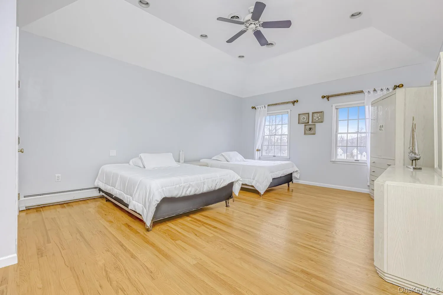 Bedroom featuring a tray ceiling, light wood finished floors, a baseboard heating unit, and a ceiling fan Bedroom featuring a tray ceiling, light wood finished floors, a baseboard heating unit, and a ceiling fan