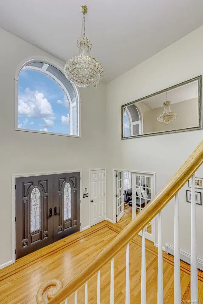 Entryway with a chandelier, wood finished floors, stairs, a towering ceiling, and a baseboard heating unit Entryway with a chandelier, wood finished floors, stairs, a towering ceiling, and a baseboard heating unit