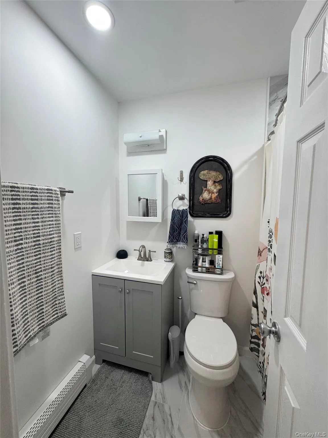Bathroom featuring baseboard heating, curtained shower, vanity, and light marble finish floors Bathroom featuring baseboard heating, curtained shower, vanity, and light marble finish floors