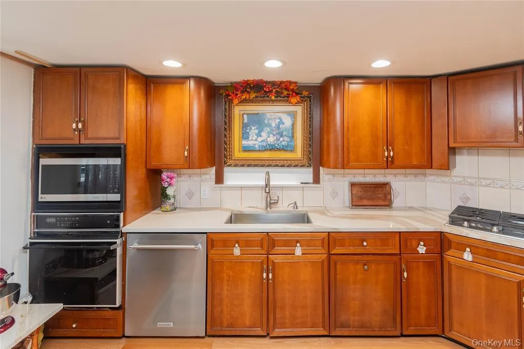 Kitchen featuring stainless steel appliances, brown cabinets, backsplash, recessed lighting, and light stone countertops Kitchen featuring stainless steel appliances, brown cabinets, backsplash, recessed lighting, and light stone countertops