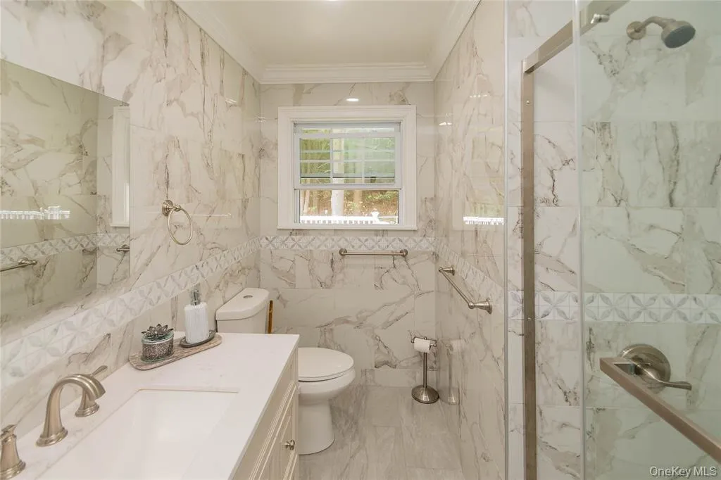 Full bath featuring tile walls, a marble finish shower, crown molding, and vanity Full bath featuring tile walls, a marble finish shower, crown molding, and vanity