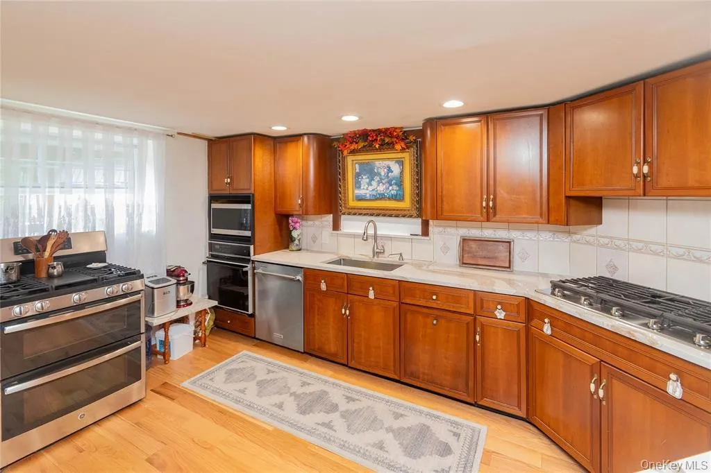 Kitchen with appliances with stainless steel finishes, brown cabinets, tasteful backsplash, light wood-style floors, and recessed lighting Kitchen with appliances with stainless steel finishes, brown cabinets, tasteful backsplash, light wood-style floors, and recessed lighting