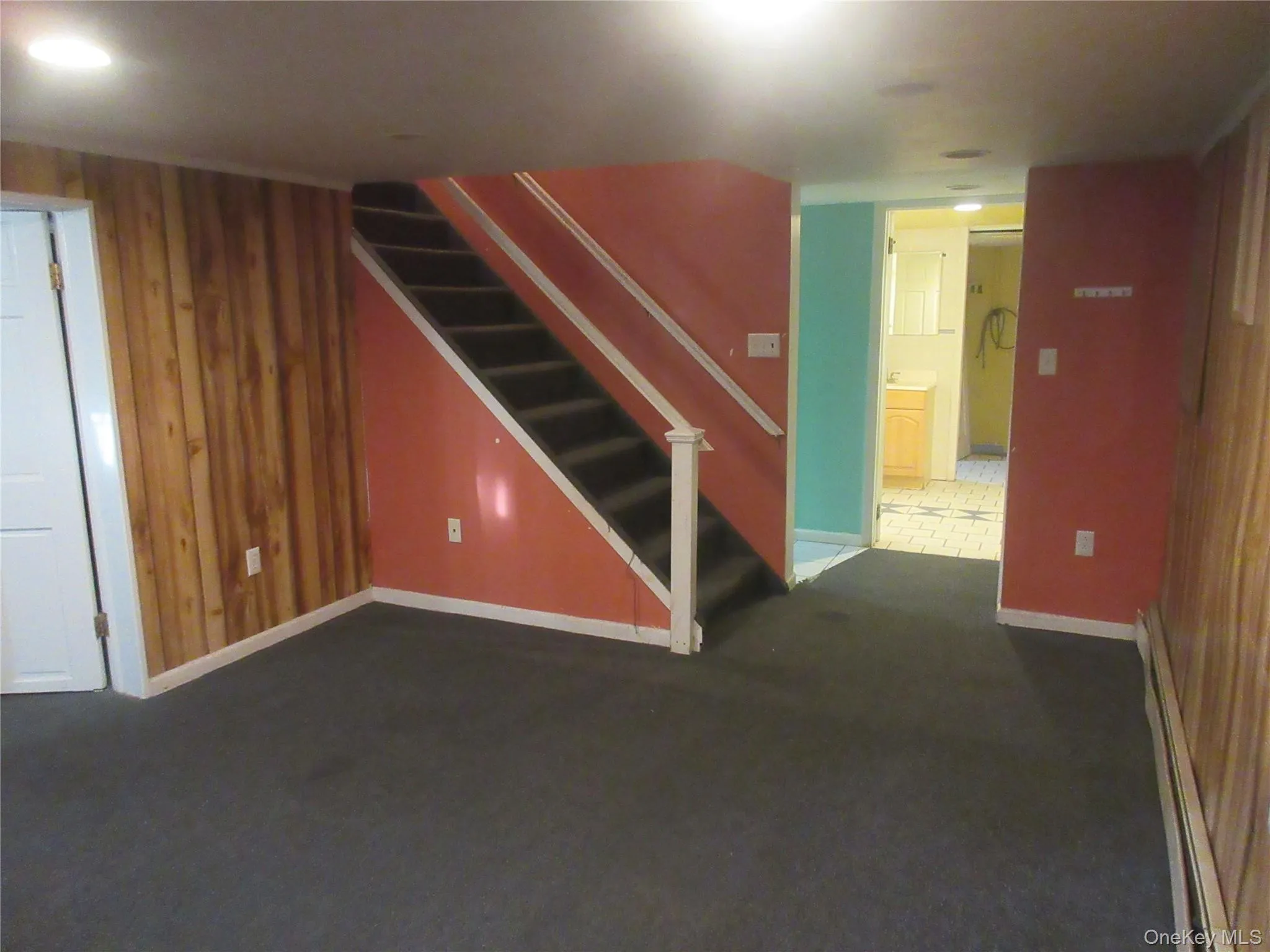Finished below grade area with wooden walls, baseboard heating, dark colored carpet, and stairs Finished below grade area with wooden walls, baseboard heating, dark colored carpet, and stairs