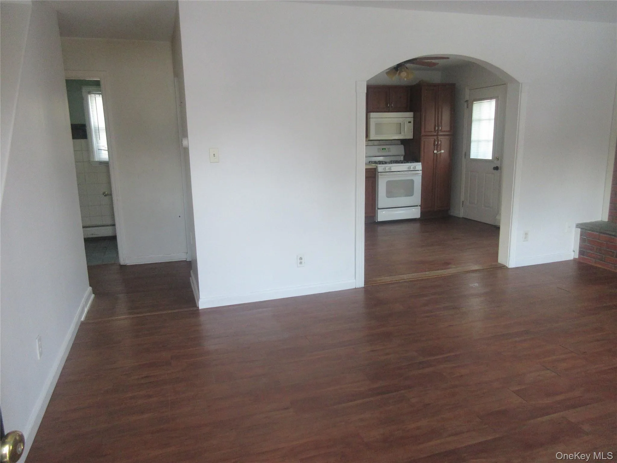 Unfurnished living room featuring arched walkways, dark wood-style flooring, and healthy amount of natural light Unfurnished living room featuring arched walkways, dark wood-style flooring, and healthy amount of natural light