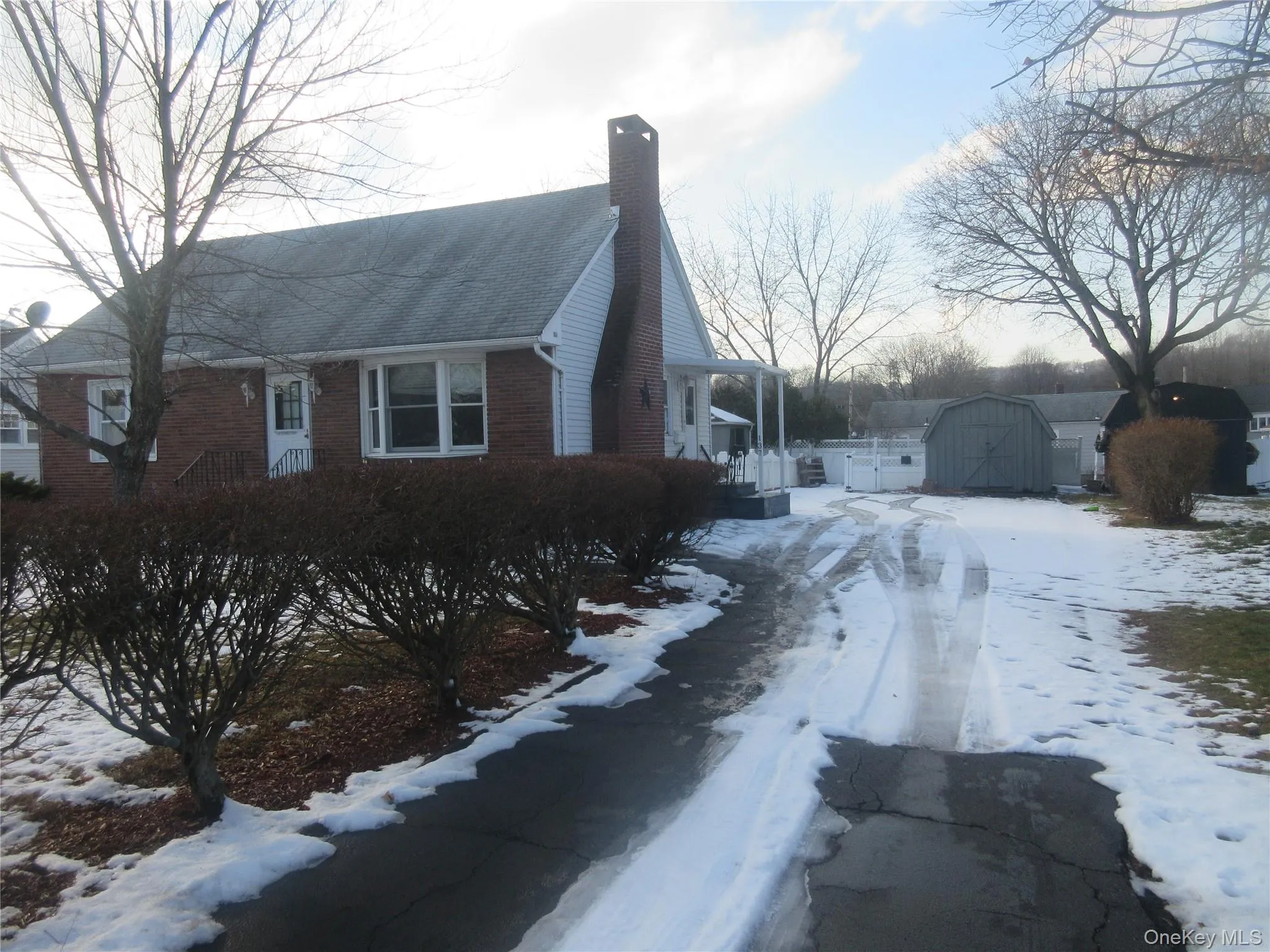 View of snowy exterior with a chimney, a shed, and brick siding View of snowy exterior with a chimney, a shed, and brick siding