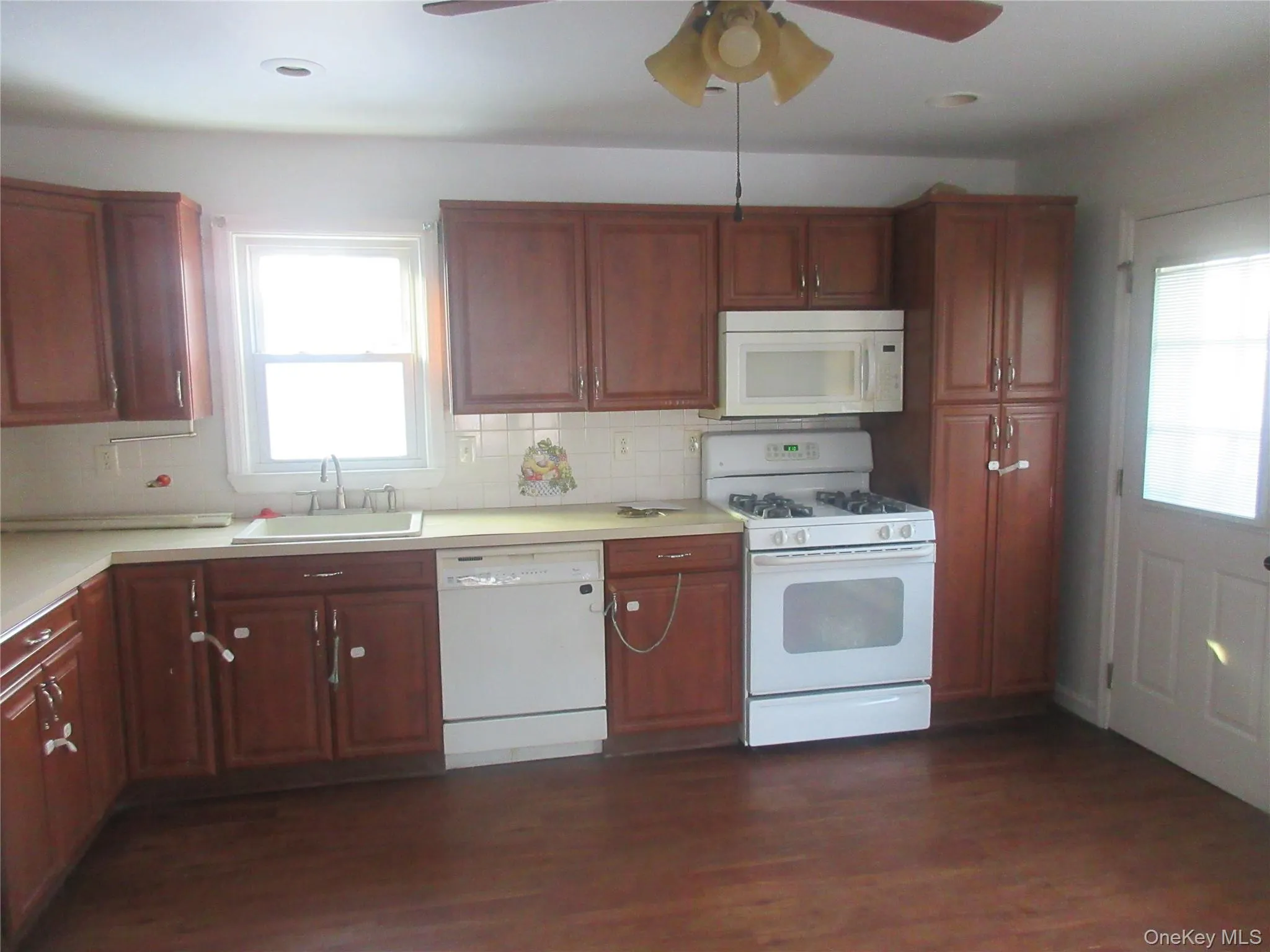 Kitchen with white appliances, light countertops, dark wood-style floors, and healthy amount of natural light Kitchen with white appliances, light countertops, dark wood-style floors, and healthy amount of natural light