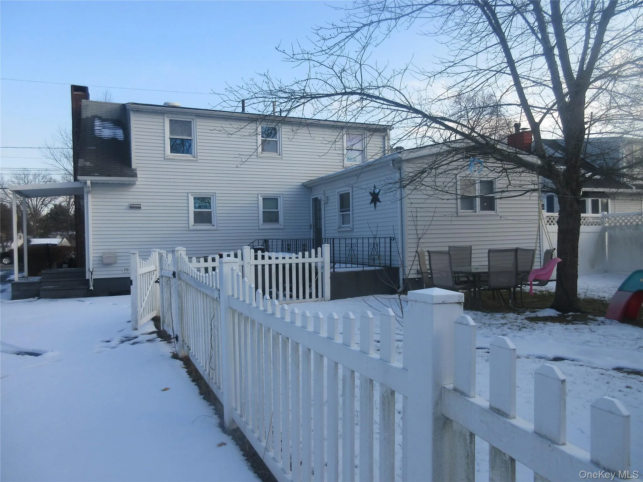 Snow covered house with a wooden deck, a fenced backyard, and a chimney Snow covered house with a wooden deck, a fenced backyard, and a chimney