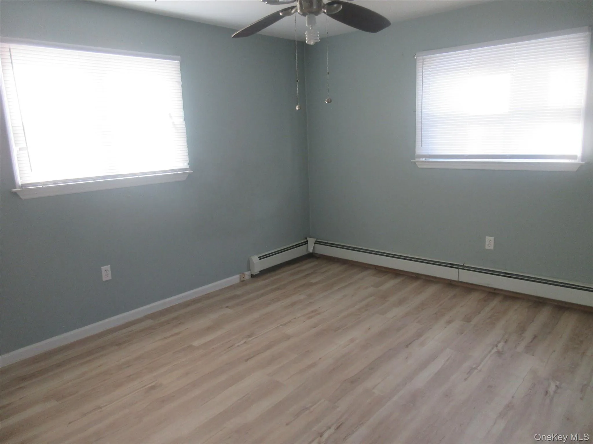 Spare room featuring light wood-style flooring, healthy amount of natural light, ceiling fan, and baseboard heating Spare room featuring light wood-style flooring, healthy amount of natural light, ceiling fan, and baseboard heating