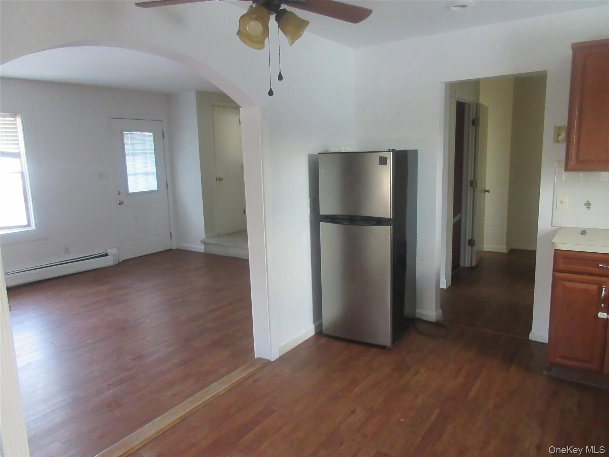 Kitchen featuring freestanding refrigerator, ceiling fan, light countertops, a baseboard heating unit, and dark wood finished floors Kitchen featuring freestanding refrigerator, ceiling fan, light countertops, a baseboard heating unit, and dark wood finished floors