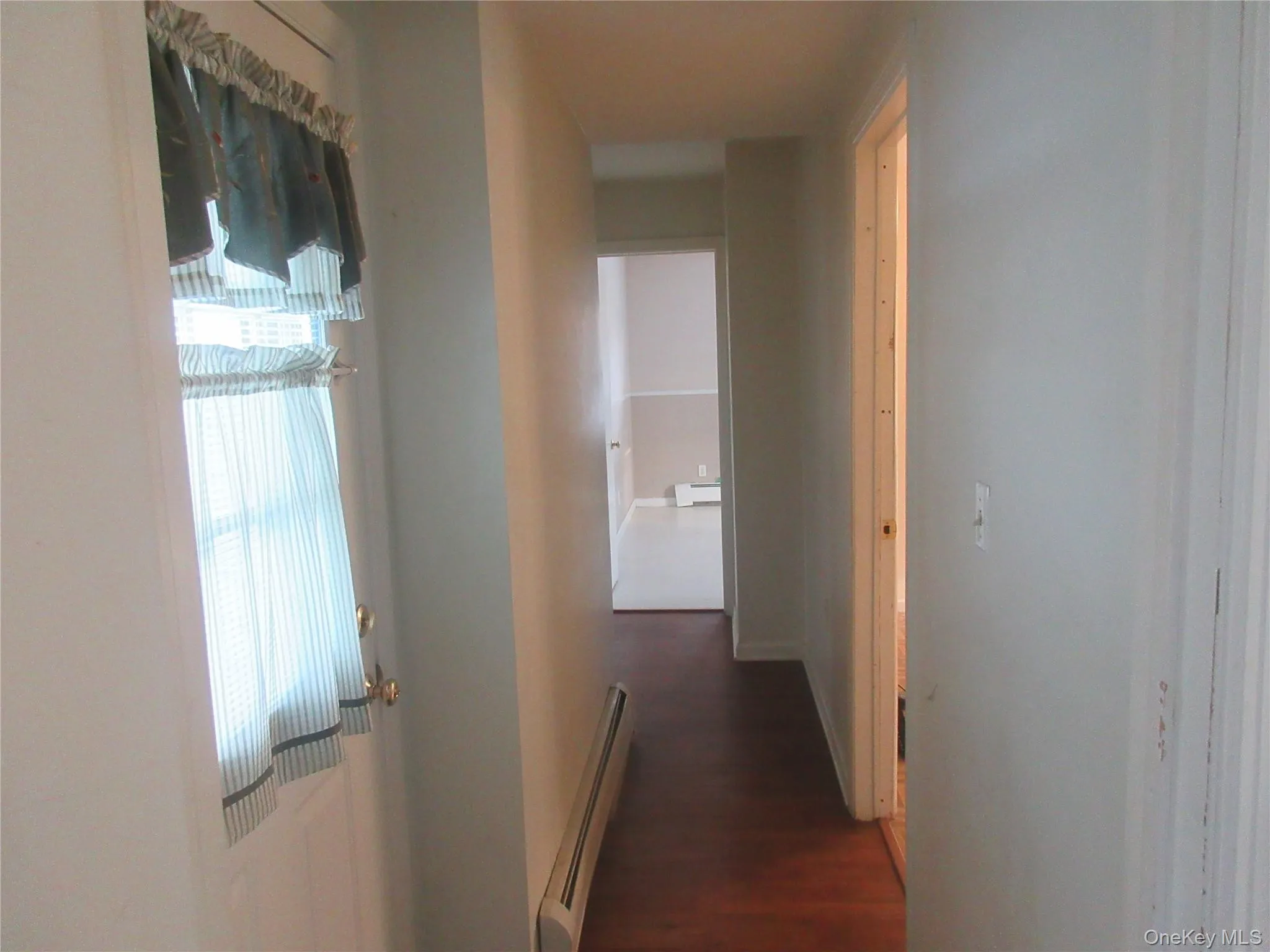 Hallway featuring baseboard heating and dark wood-style flooring Hallway featuring baseboard heating and dark wood-style flooring