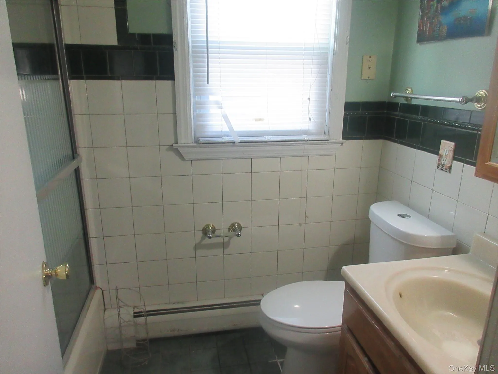 Full bath with a baseboard heating unit, dark tile patterned floors, vanity, and tile walls Full bath with a baseboard heating unit, dark tile patterned floors, vanity, and tile walls